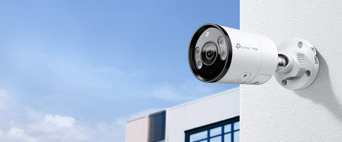 Camera op een wandbeugel tegen de gevel van een licht gebouw, met blauwe lucht erachter