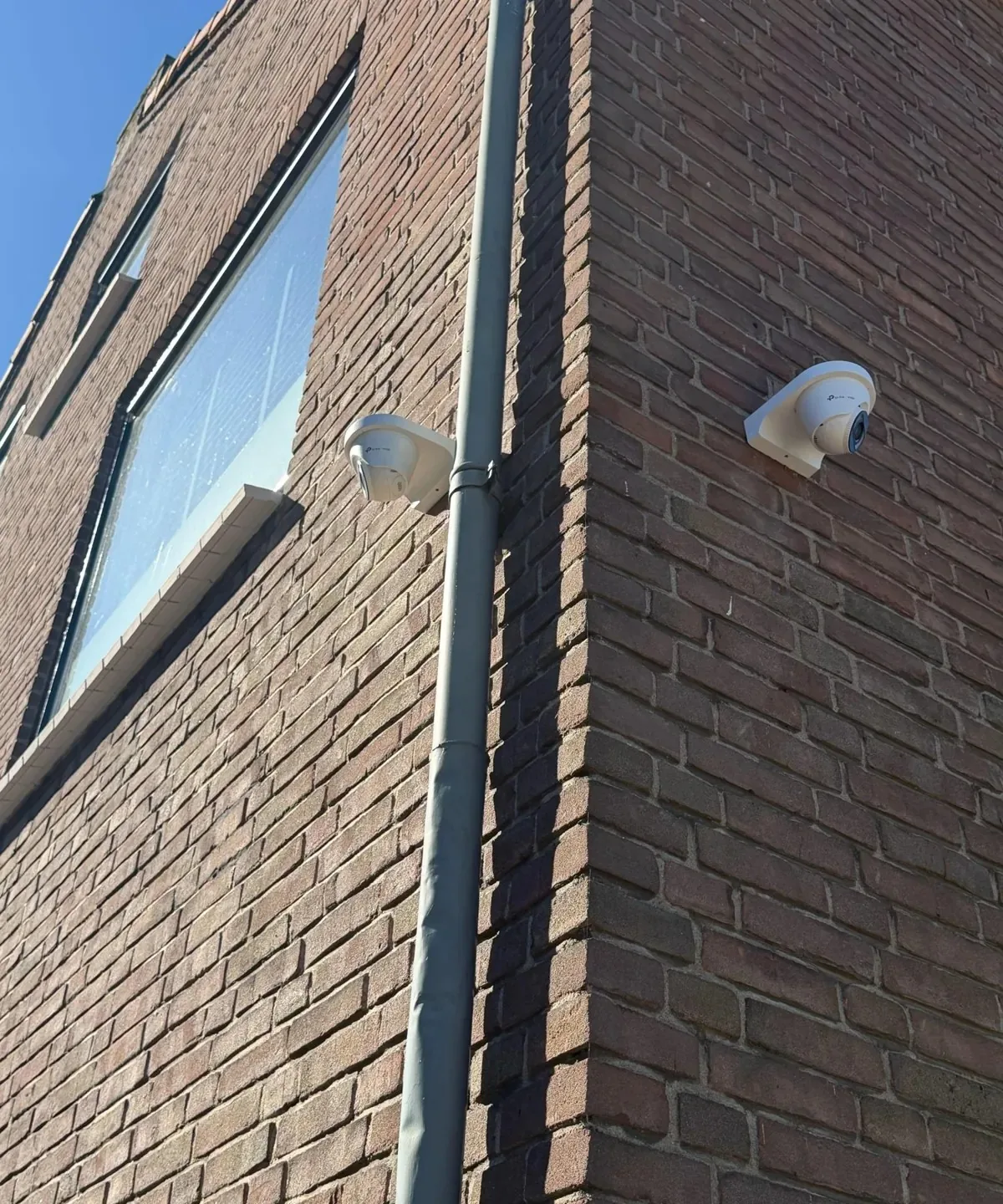 Twee witte VIGI-turretcamera’s op de hoek van een bakstenen gevel, elk naar een andere kant gericht
