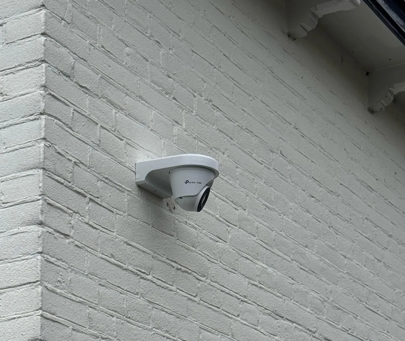 Witte VIGI-turretcamera op een wit geschilderde bakstenen gevel, met het VIGI-logo op de zijkant