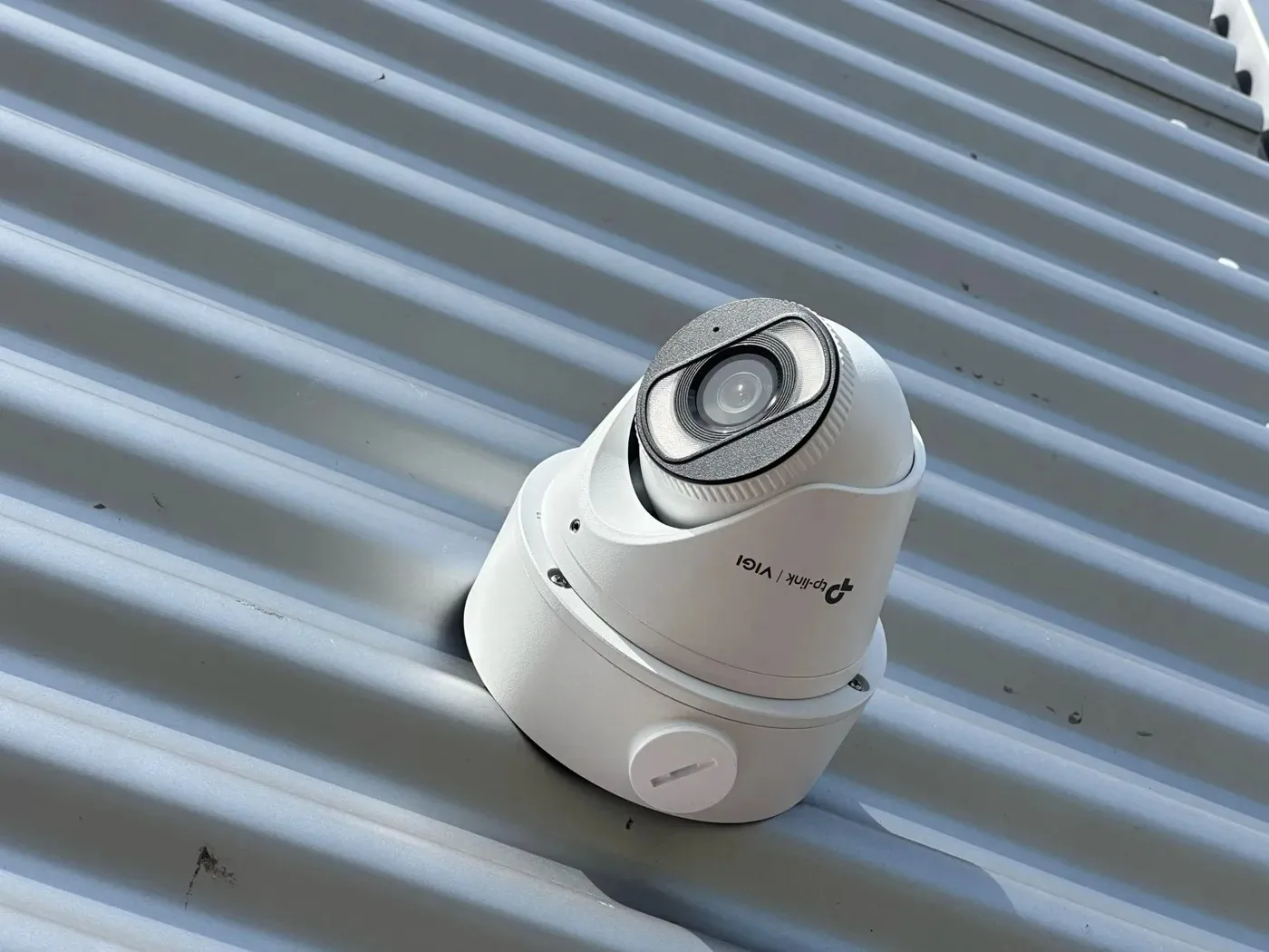 Witte VIGI-turretcamera van dichtbij tegen een grijze damwand, met tp-link VIGI op de voet