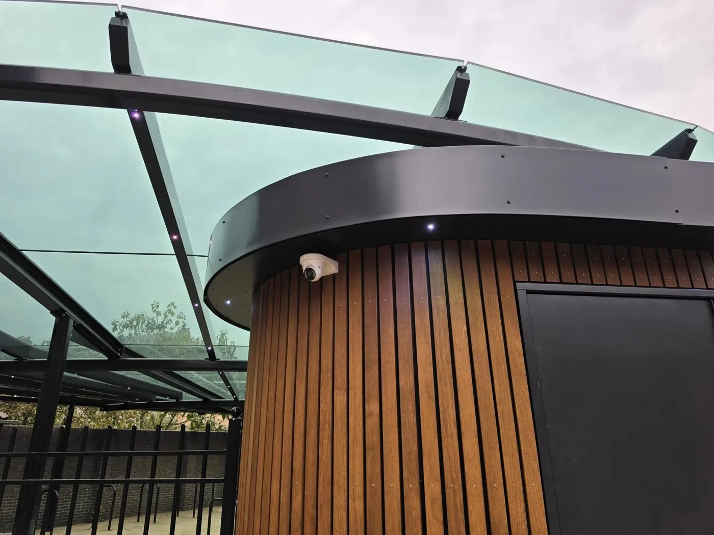 Rond houten beheerdershuisje onder een glazen overkapping, met een witte VIGI-turret onder de dakrand